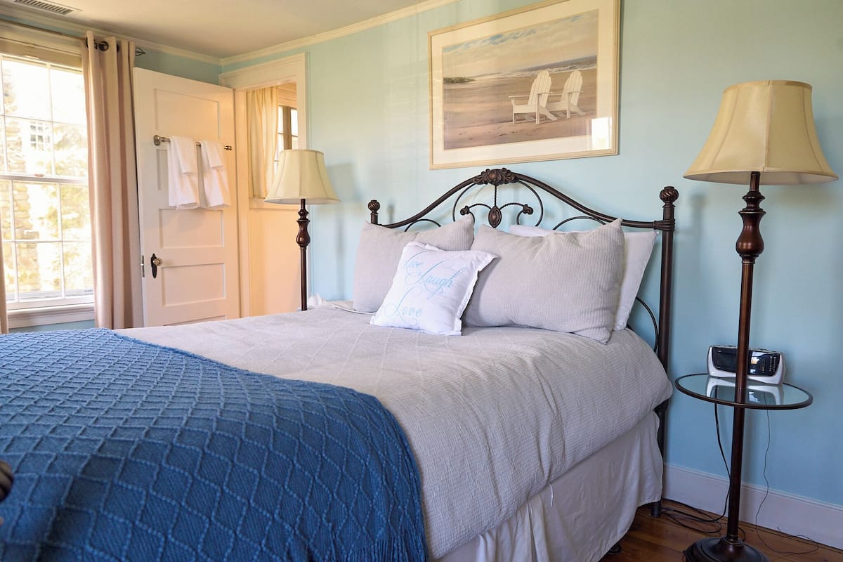 A bedroom with a bed, two bedside lamps, a small table, and a painting on the wall.