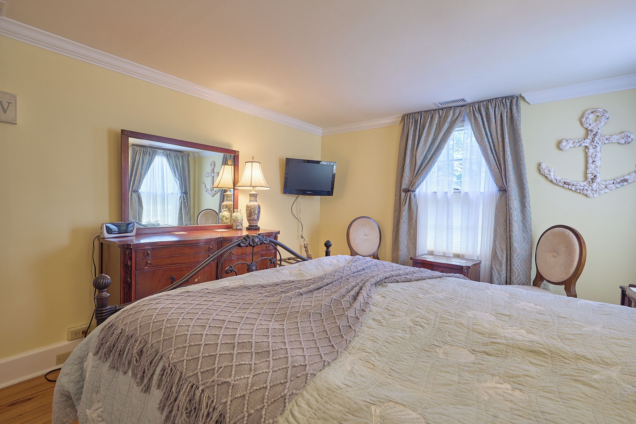A bedroom with a bed, dresser, mirror, television, and curtains.