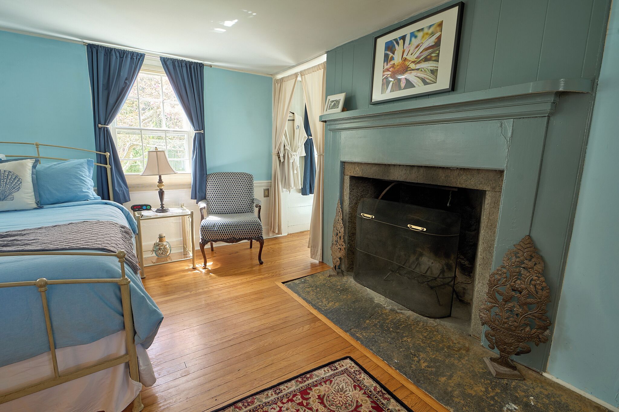 A bedroom with a bed, a chair, a fireplace, and a window with curtains.