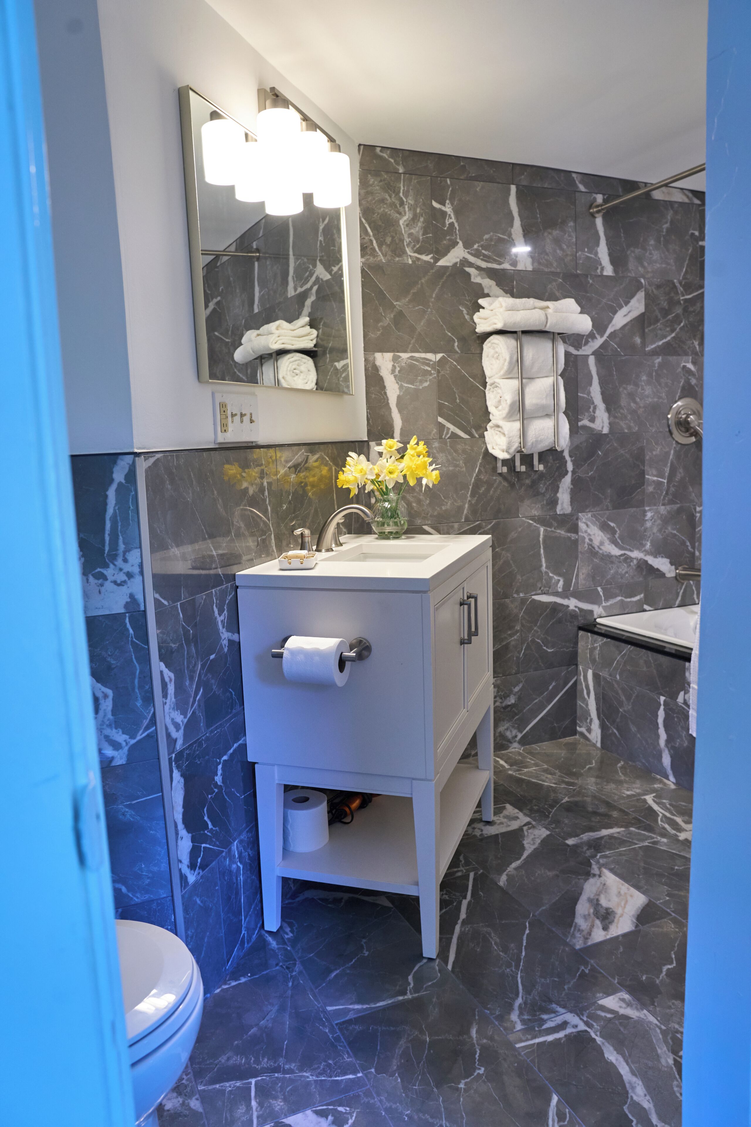 A bathroom with marble walls, a white sink, a mirror, and a toilet.