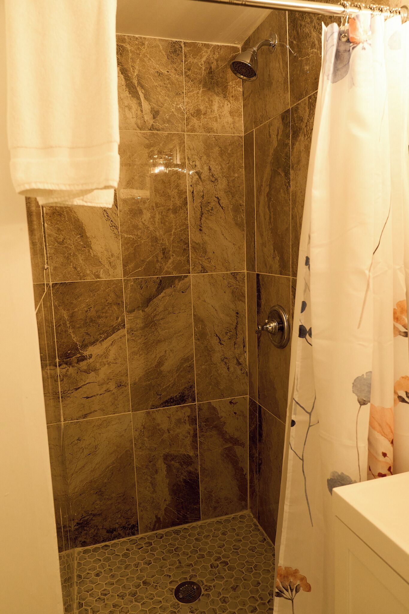 A shower with a glass door, a showerhead, and a tiled wall.