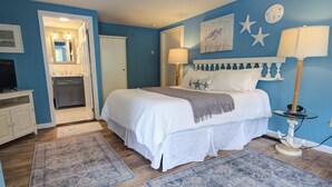 A bedroom with a bed, two rugs, a nightstand, a lamp, and a wall clock. - The Scranton Seahorse Inn (Madison)
