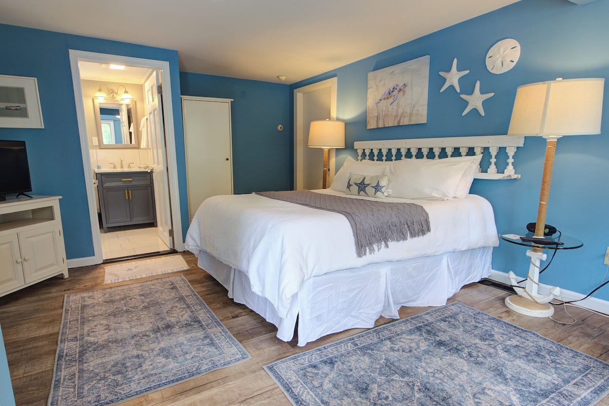 A bedroom with a bed, two rugs, a nightstand, a lamp, and a wall clock.