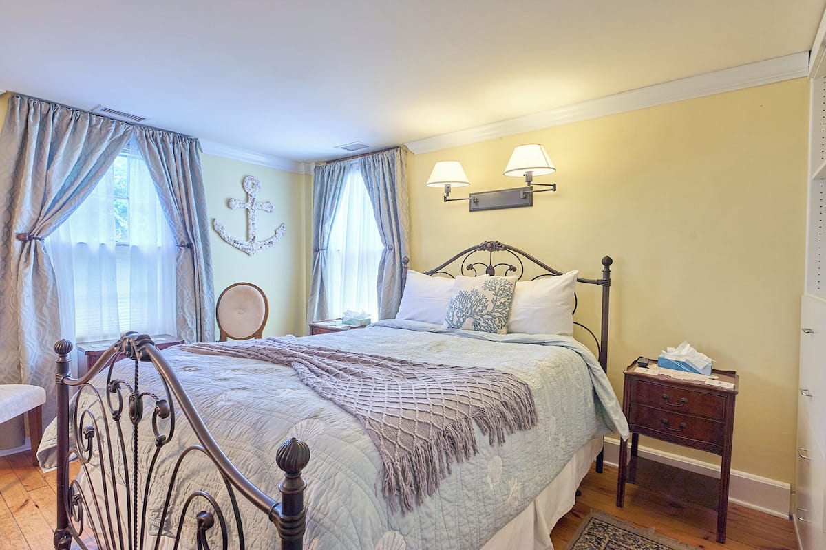A bedroom with a bed, curtains, a nightstand, a lamp, and a wall-mounted light fixture.