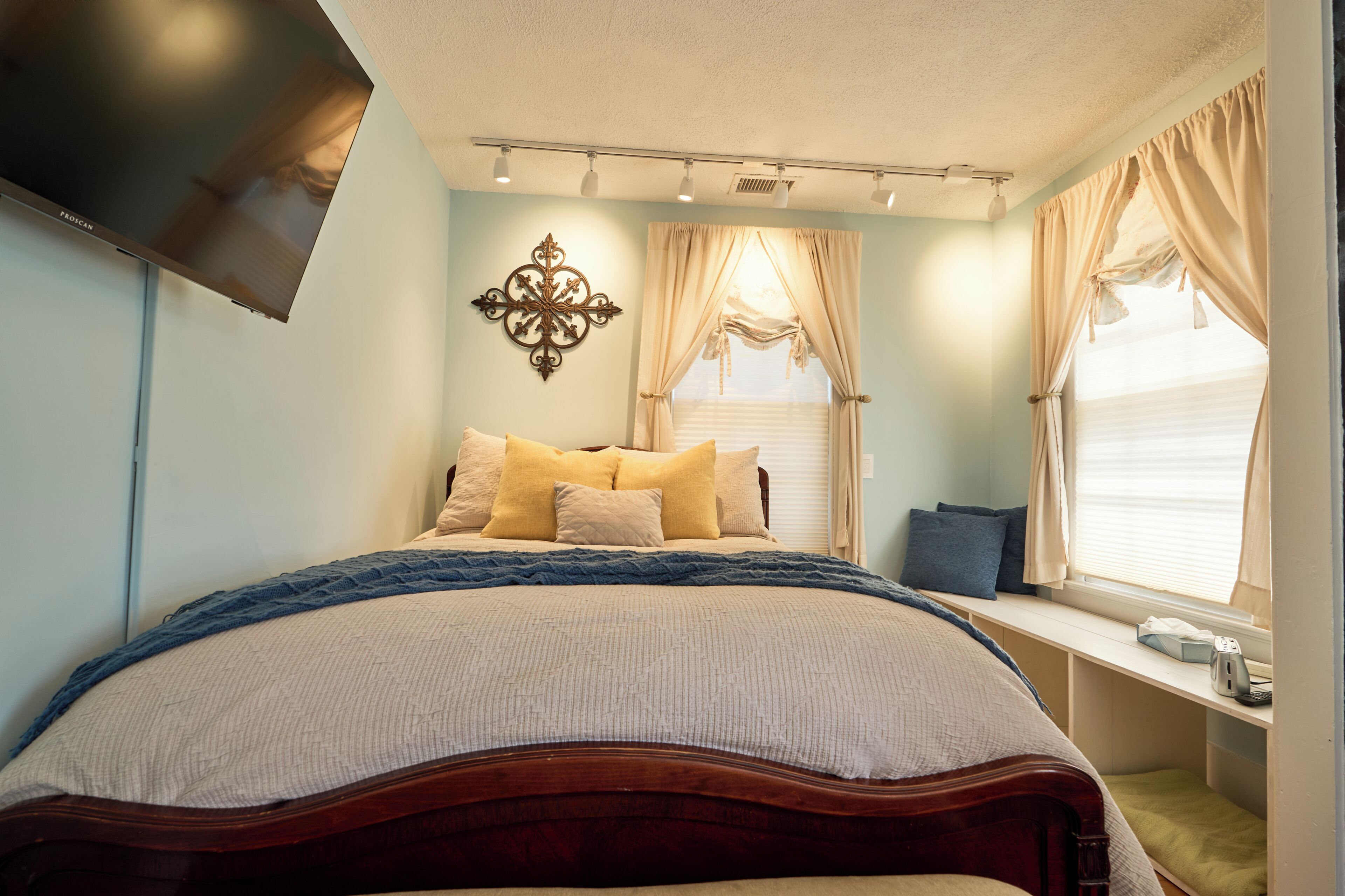 A bedroom with a bed, a TV mounted on the wall, a window with curtains, and a bedside table.