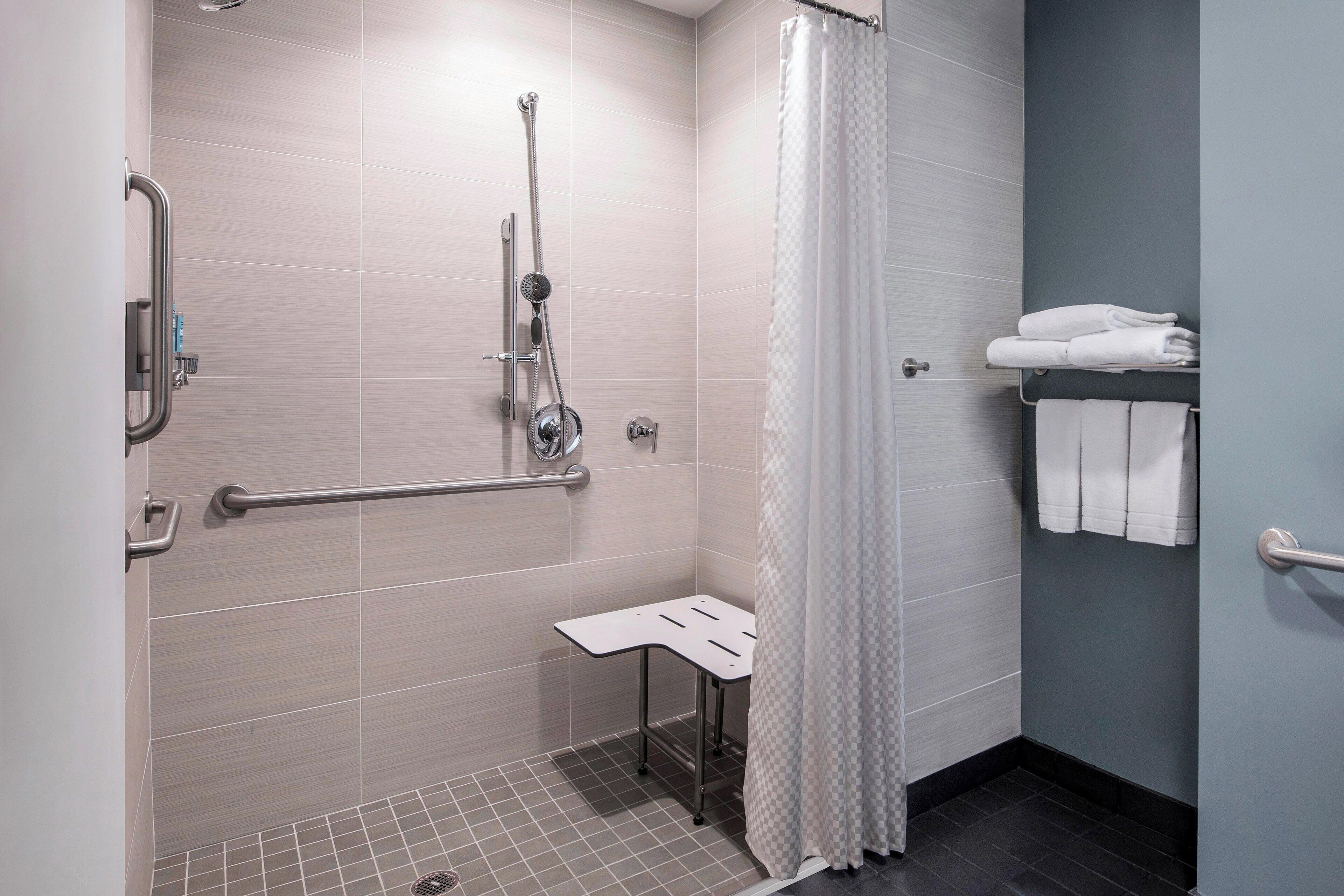 A modern bathroom with a shower, grab bars, a small table, and a towel rack.