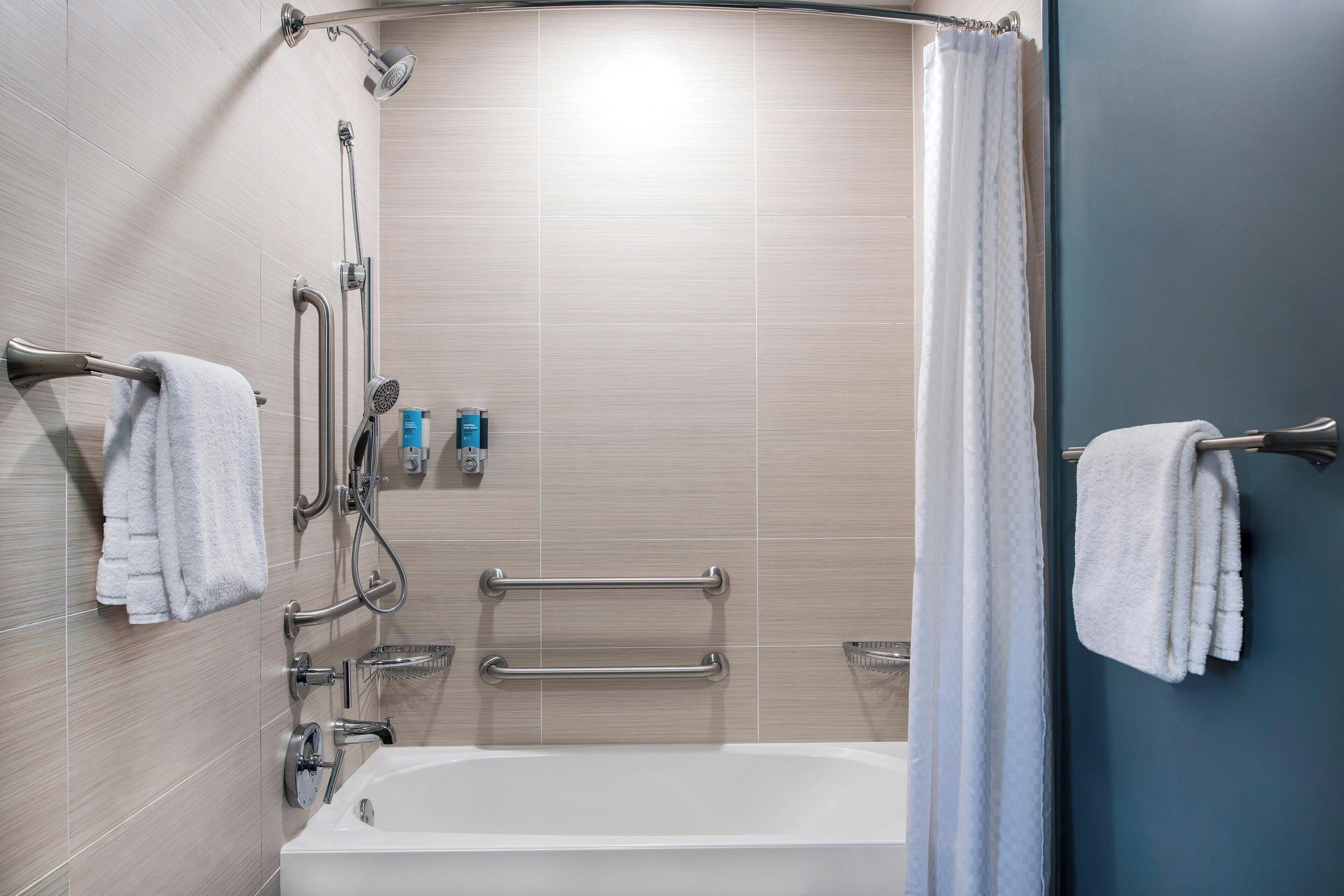 A modern bathroom with a bathtub, grab bars, and a shower area.