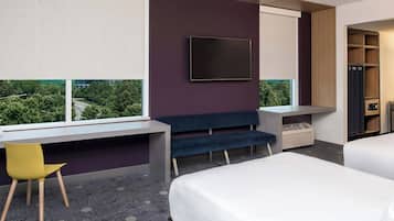 Una habitación de hotel moderna con una cama grande, un escritorio con silla, un televisor montado en la pared y vistas a zonas verdes.