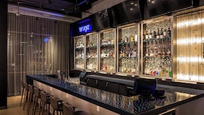 A bar area with a long counter, multiple stools, and shelves stocked with bottles.