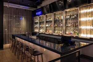 Un espace bar doté d’un long comptoir, de nombreux tabourets et d’étagères remplies de bouteilles.