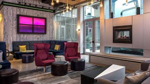A modern lounge area with a sofa, armchairs, and ottomans, a fireplace, and large windows.