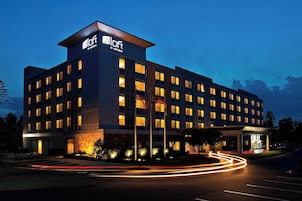 A modern hotel building with a prominent 'Aloft Hotels' sign, multiple floors, and a well-lit entrance.