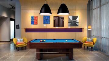 A pool table with two yellow armchairs, wooden paneling, and artwork on the wall.