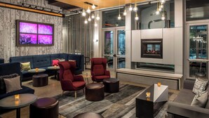 A modern lounge area with a sofa, armchairs, and round tables, featuring a fireplace and large windows.