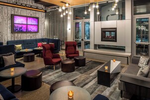 Un espace de détente moderne comprenant un canapé, des fauteuils et des tables rondes, avec une cheminée et de grandes fenêtres.