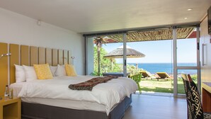 Quarto com uma cama grande, uma mesa de cabeceira e vista para o mar através de uma porta de vidro deslizante.