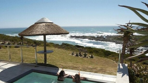 Piscina com vista para o oceano e um guarda-sol de palha.