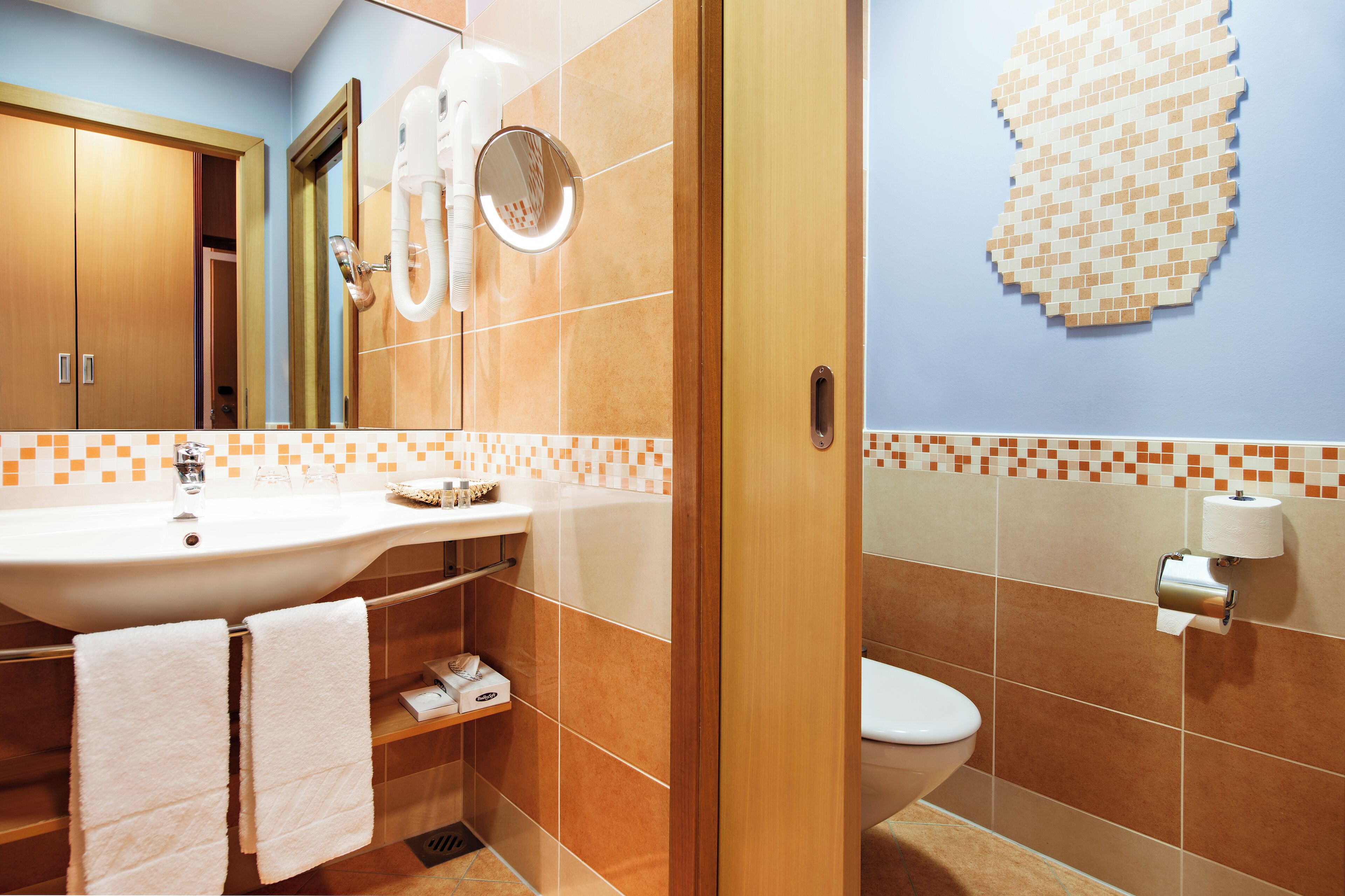 A bathroom with a sink, mirror, towel rack, toilet, and a wall-mounted toilet paper holder.
