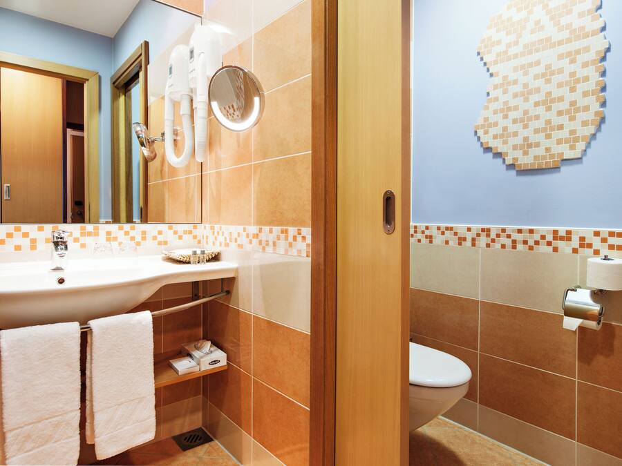 A bathroom with a sink, mirror, towel rack, toilet, and a wall-mounted toilet paper holder.