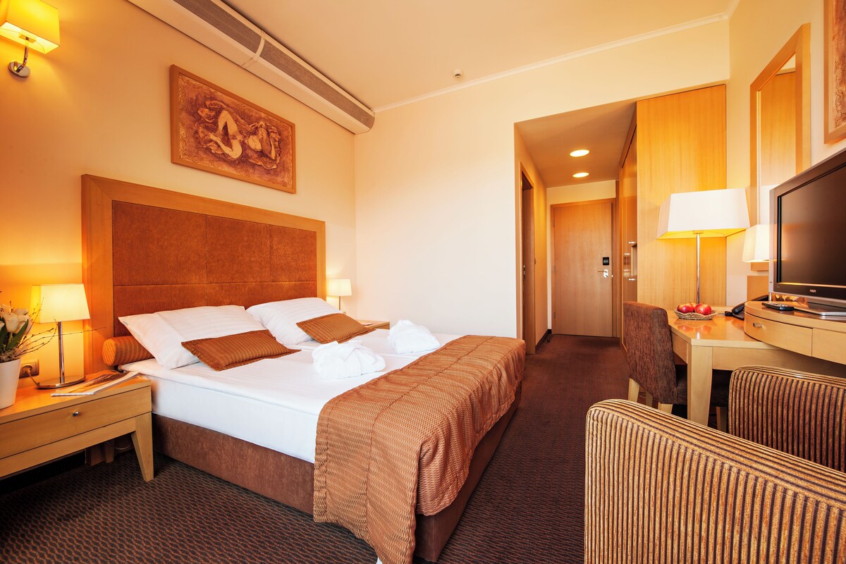 A hotel room with a large bed, a desk with a television, and a dining area.