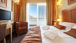 A hotel room with a bed, a desk with a television, a chair, and a view of the outdoors through a large window. - Grand Hotel Primus - Sava Hotels & Resorts (Ptuj)