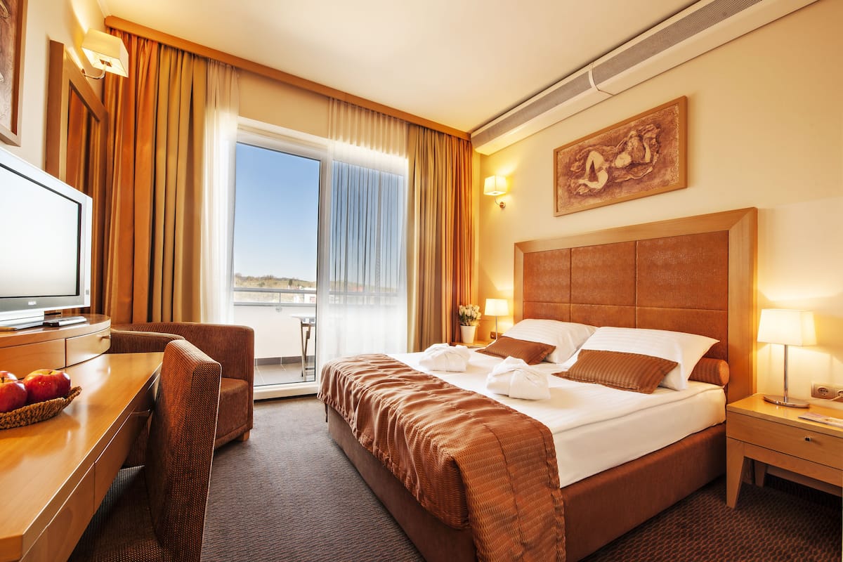 Ein Hotelzimmer mit einem großen Bett, einem Schreibtisch mit Fernseher und Blick ins Freie durch eine Schiebetür.