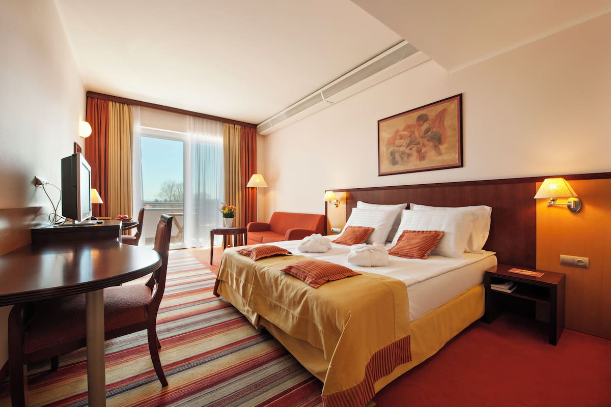 Ein Hotelzimmer mit Bett, Schreibtisch, Stuhl, Lampe und einem Gemälde an der Wand.