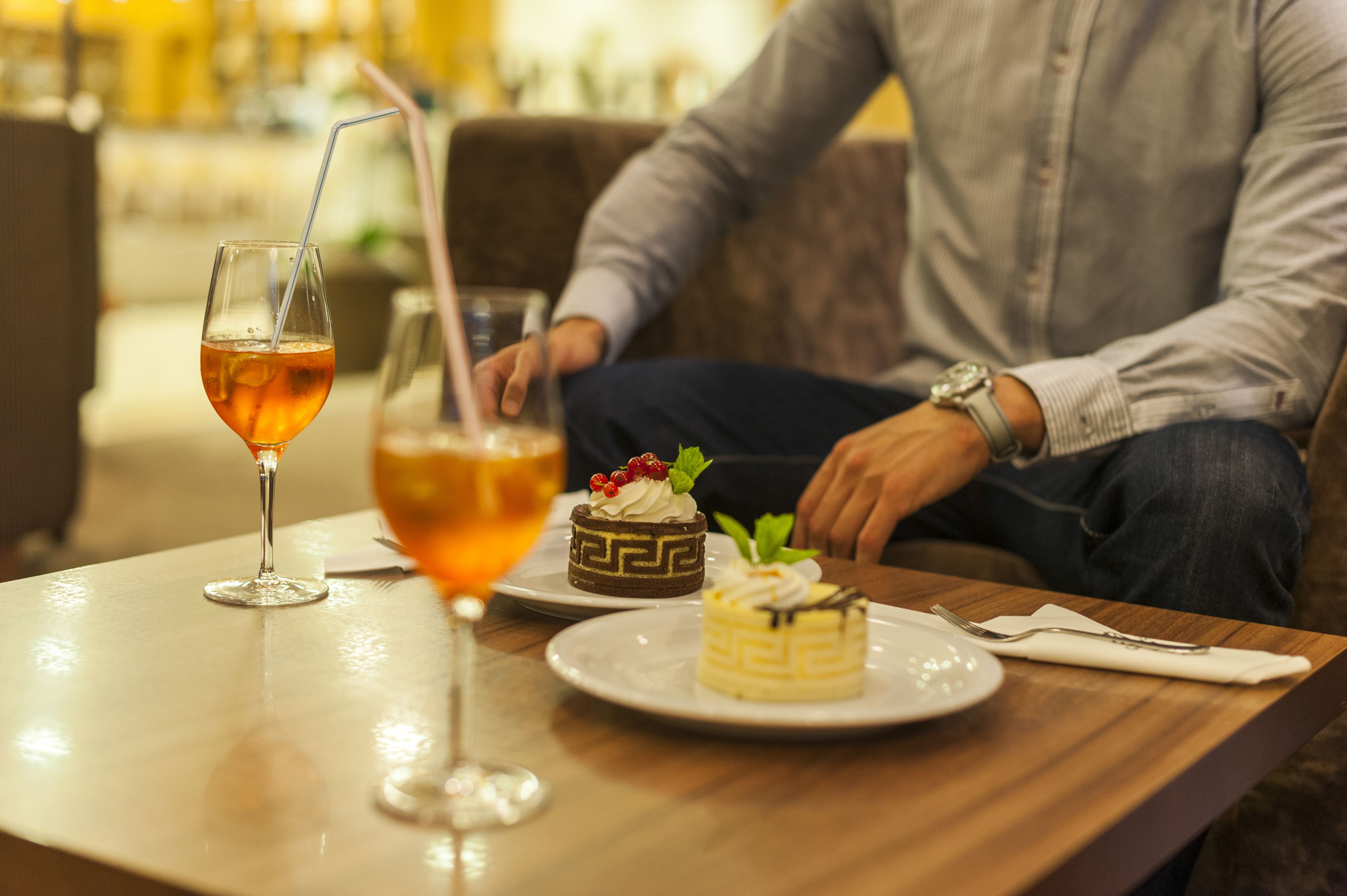 Une table de restaurant avec une boisson ambrée dans un verre, deux petits desserts et une fourchette, le tout posé sur une table en bois.