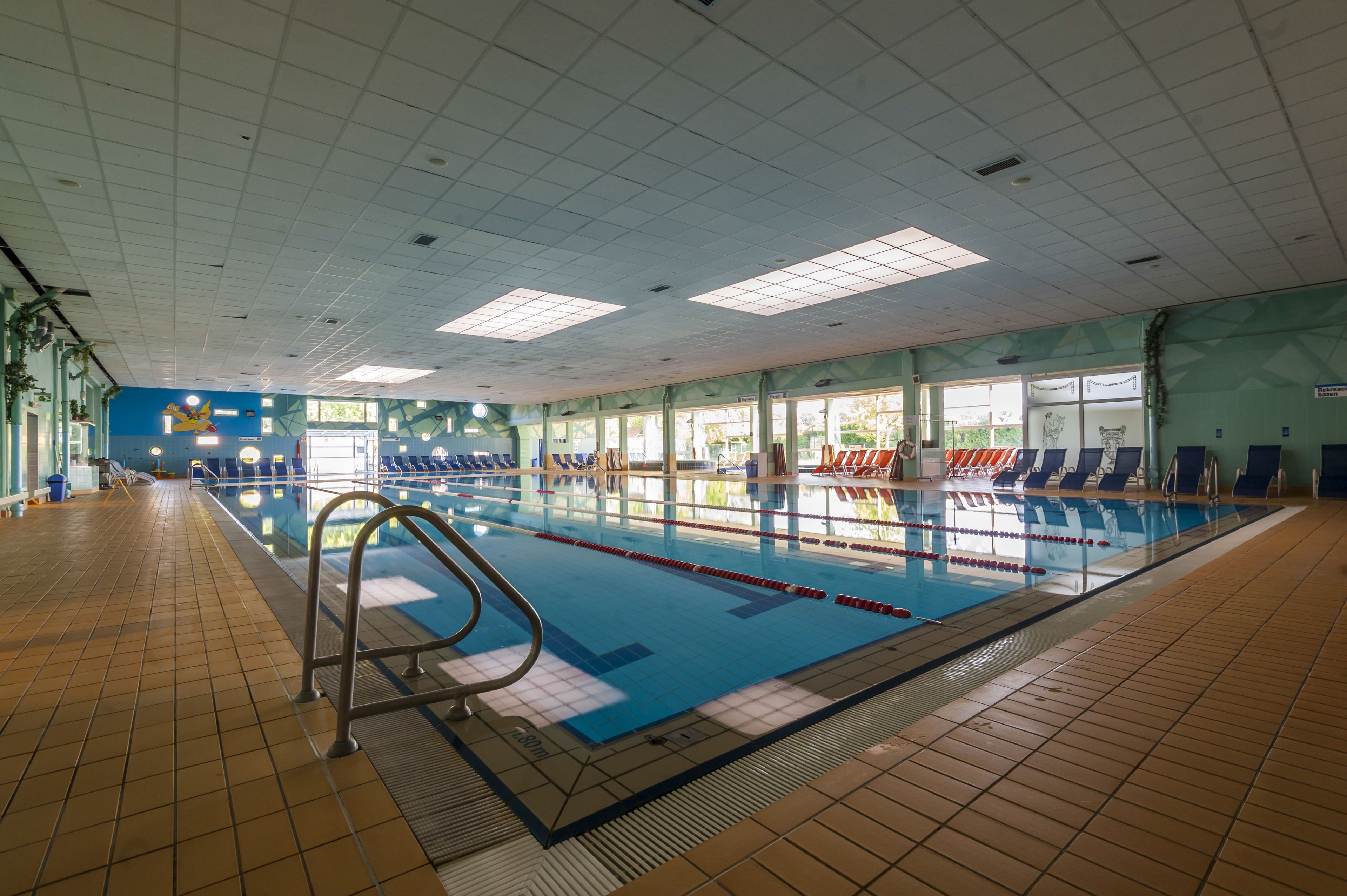 An indoor swimming pool with clear lanes, a tiled floor, and a blue wall with a logo.