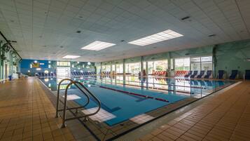 An indoor swimming pool with clear lanes, a tiled floor, and a blue wall with a logo.