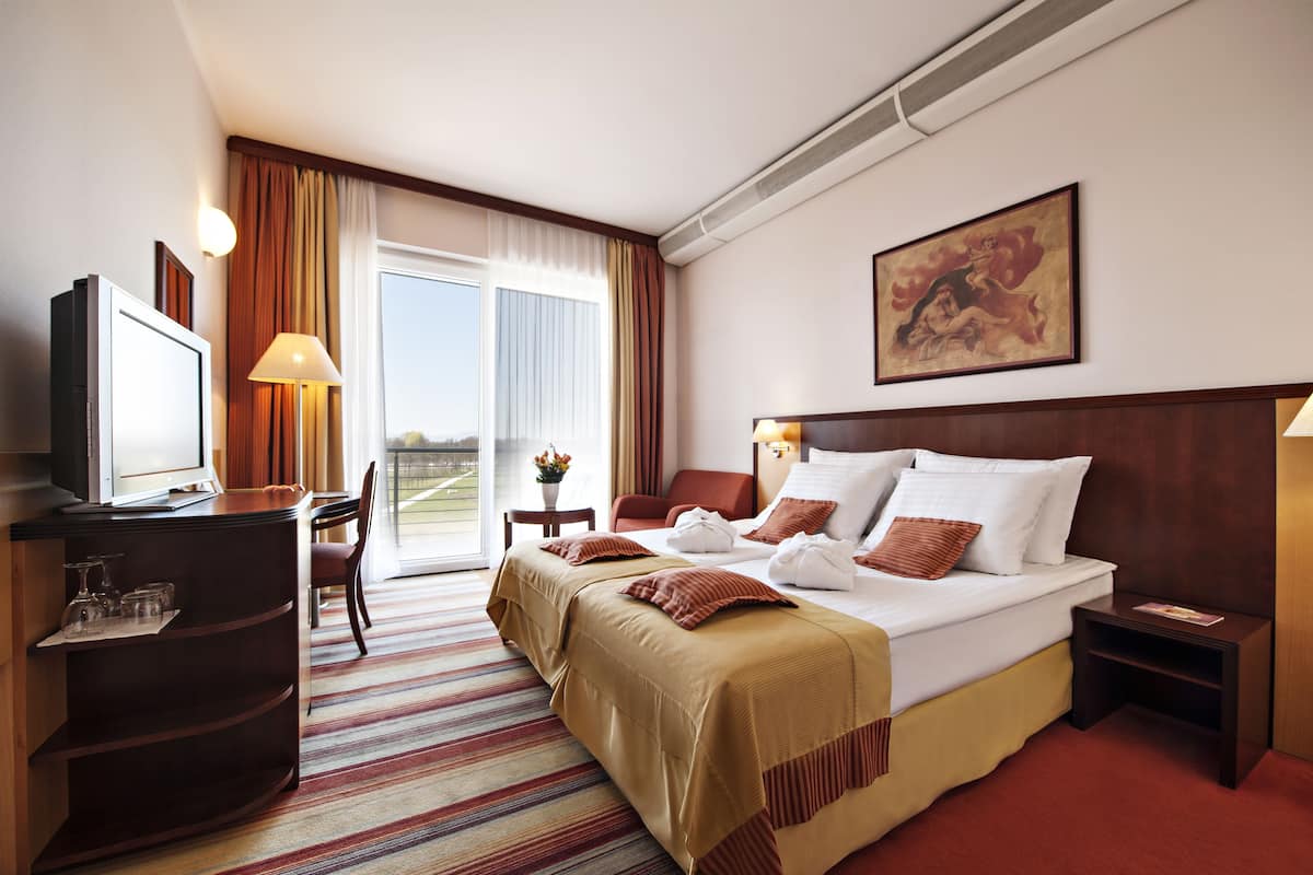 Ein Hotelzimmer mit Bett, Schreibtisch, Stuhl, Fernseher und einem Fenster mit Vorhängen.