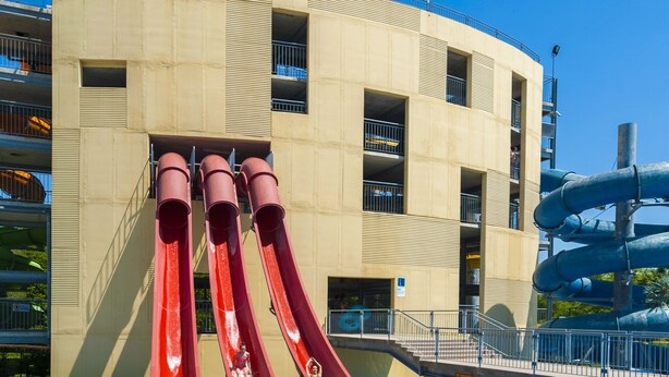 A pool with three red slides and a water park structure in the background. - Grand Hotel Primus - Sava Hotels & Resorts (Ptuj)