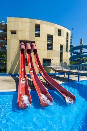Una piscina con tres toboganes rojos y una estructura de parque acuático al fondo.