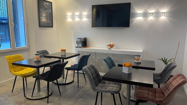 A modern dining area with a flat-screen TV mounted on the wall, a coffee machine, and a bowl of oranges on the counter. - Hotel Anna Livia (Cannes)