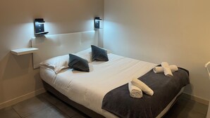 A neatly made bed with pillows, a bedside table with a lamp, and a towel on the bed. - Hotel Anna Livia (Cannes)
