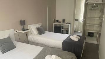 A hotel room with two beds, a desk, a mirror, and a wardrobe.