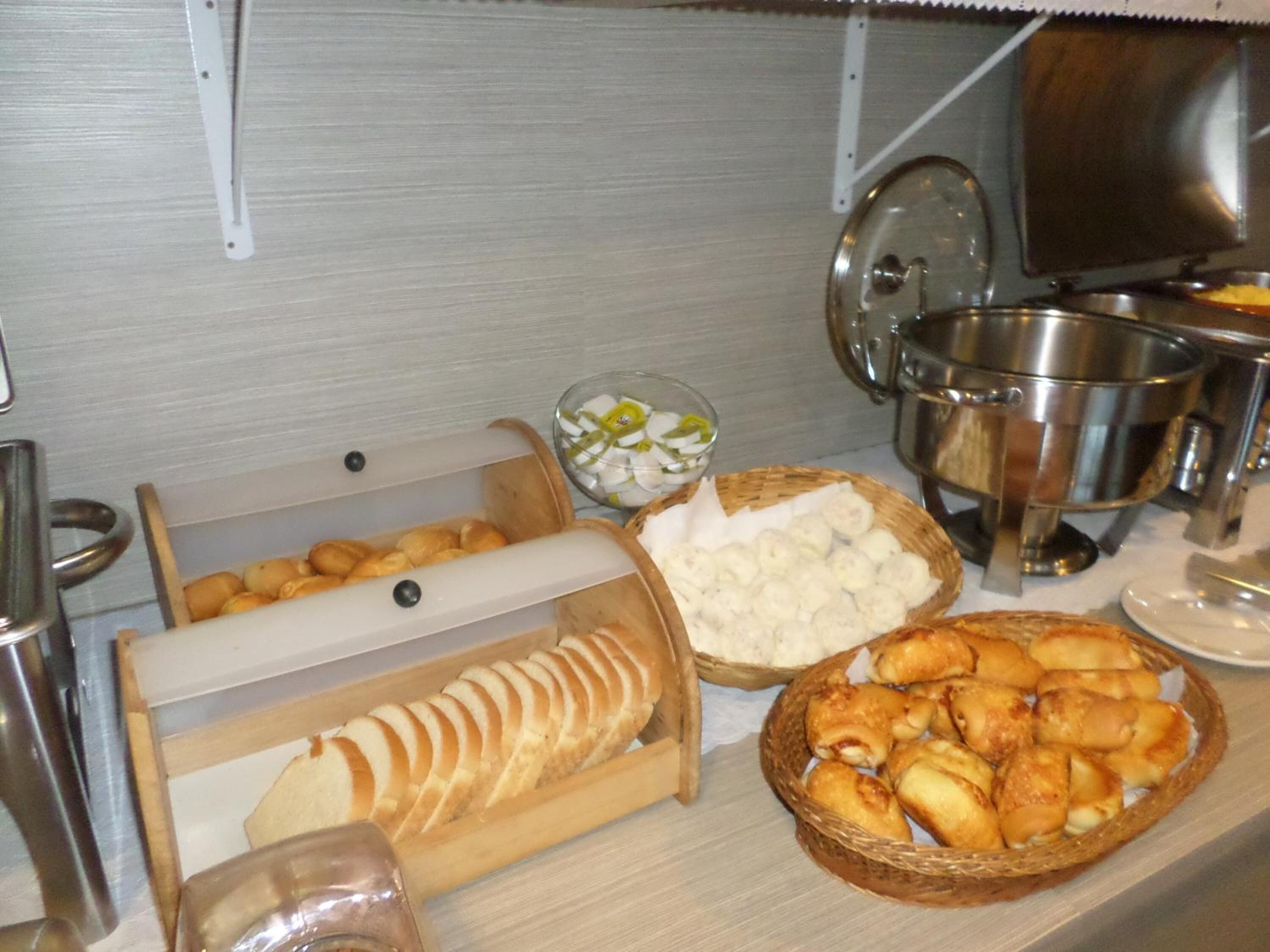 A buffet setup with various food items including bread, pastries, and a bowl of white food, possibly cheese or dip.