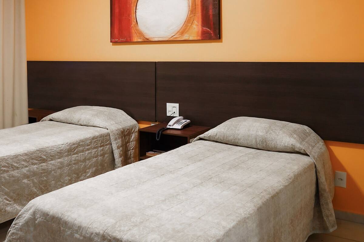 Een hotelkamer met twee bedden, een nachtkastje, een telefoon en een schilderij aan de muur.