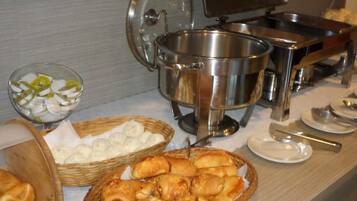 A buffet setup with various food items, including baskets of pastries and a bowl of sliced fruit.