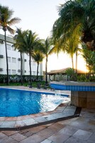 Una piscina con una fuente, rodeada de palmeras y un edificio blanco con unidades de aire acondicionado.