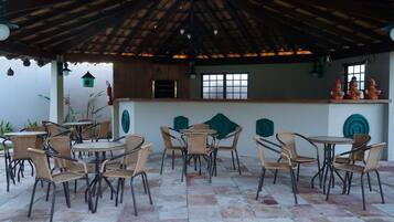 An outdoor patio area with wicker furniture, a thatched roof, and decorative pottery.
