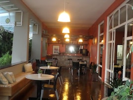 Un restaurante acogedor con una barra alargada, varias mesas y sillas. Hay luces colgantes y un amplio ventanal a la derecha.