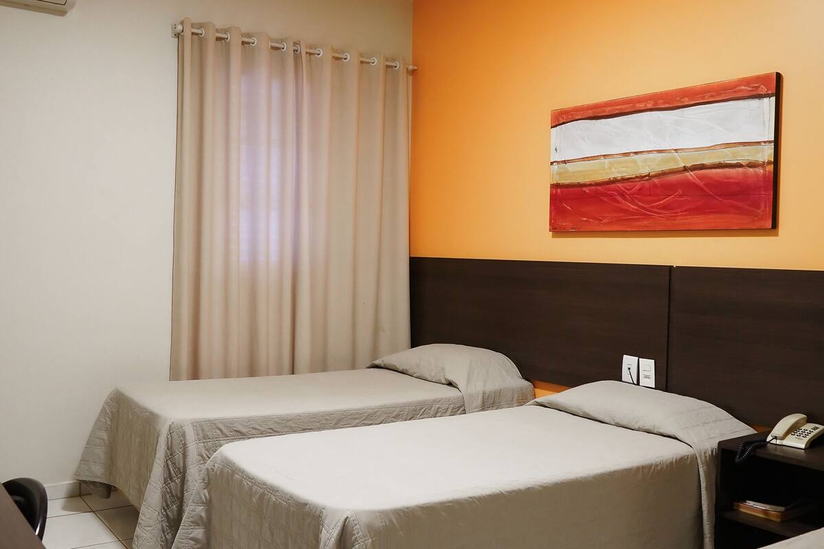 Een hotelkamer met twee bedden, een bureau, een airconditioner en een schilderij aan de muur.