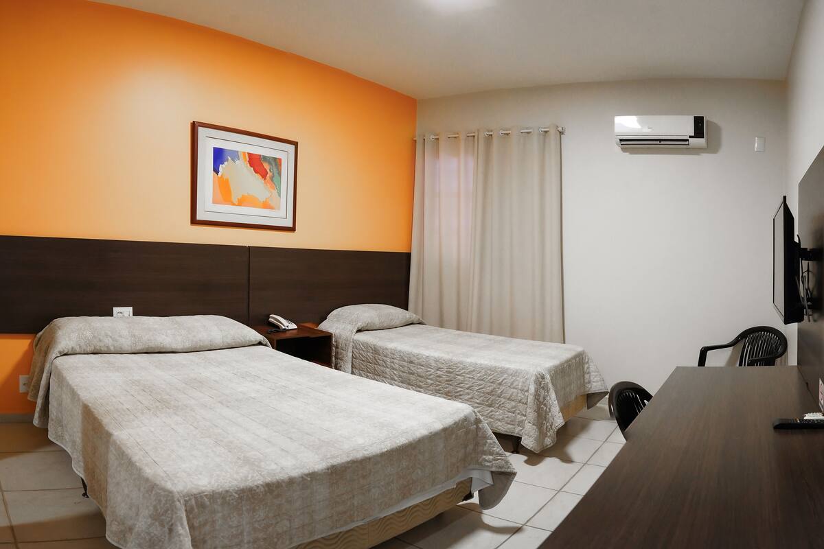 Een hotelkamer met twee bedden, een bureau, een stoel, een televisie en een airconditioning.