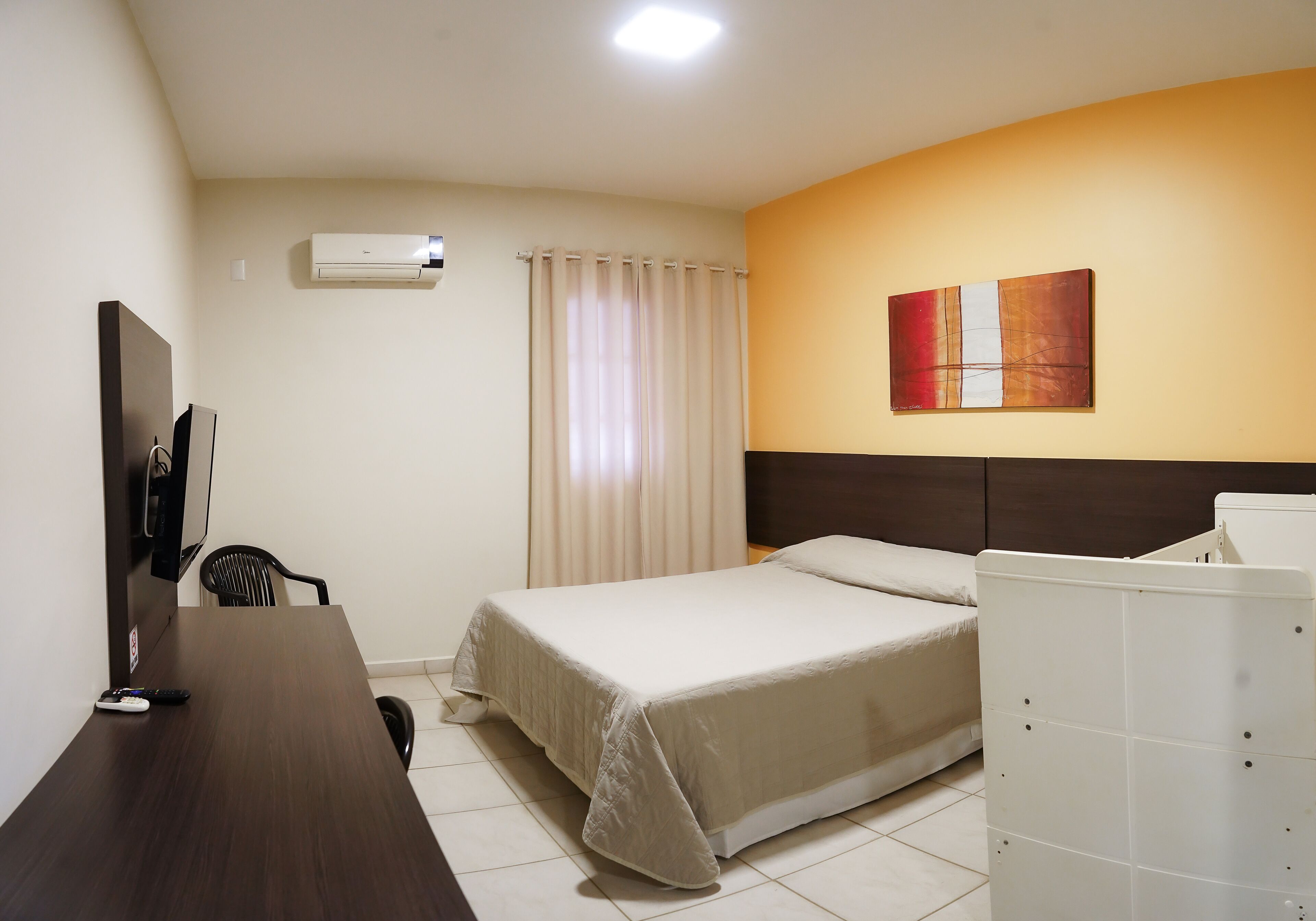 Habitación de hotel con cama, escritorio, silla, aire acondicionado y un cuadro en la pared.