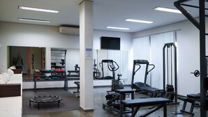 A gym with exercise equipment, a mirror, and a television on the wall.