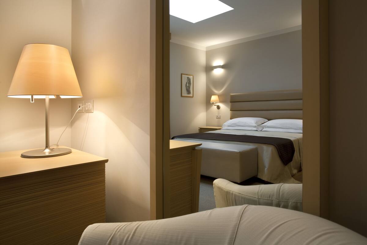A hotel room with a bed, bedside lamp, and a desk with a lamp.