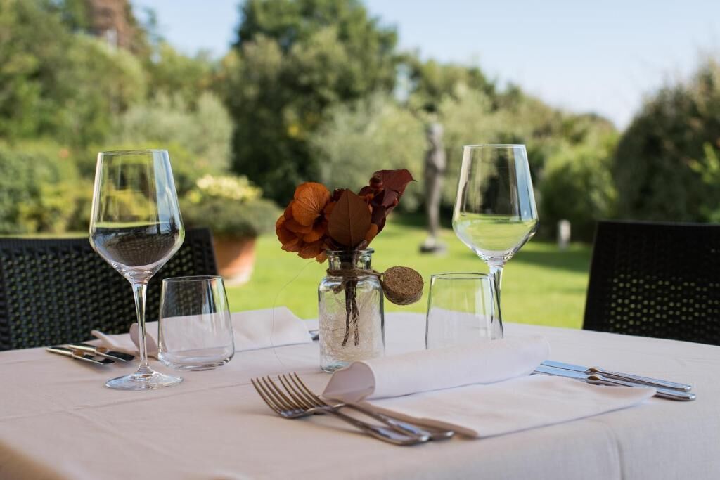 Una mesa al aire libre con copas de vino, un jarrón con flores secas y un frasco pequeño con tapón de corcho.