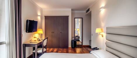 Una habitación de hotel con cama, escritorio, silla, televisor y puerta que da a un baño.