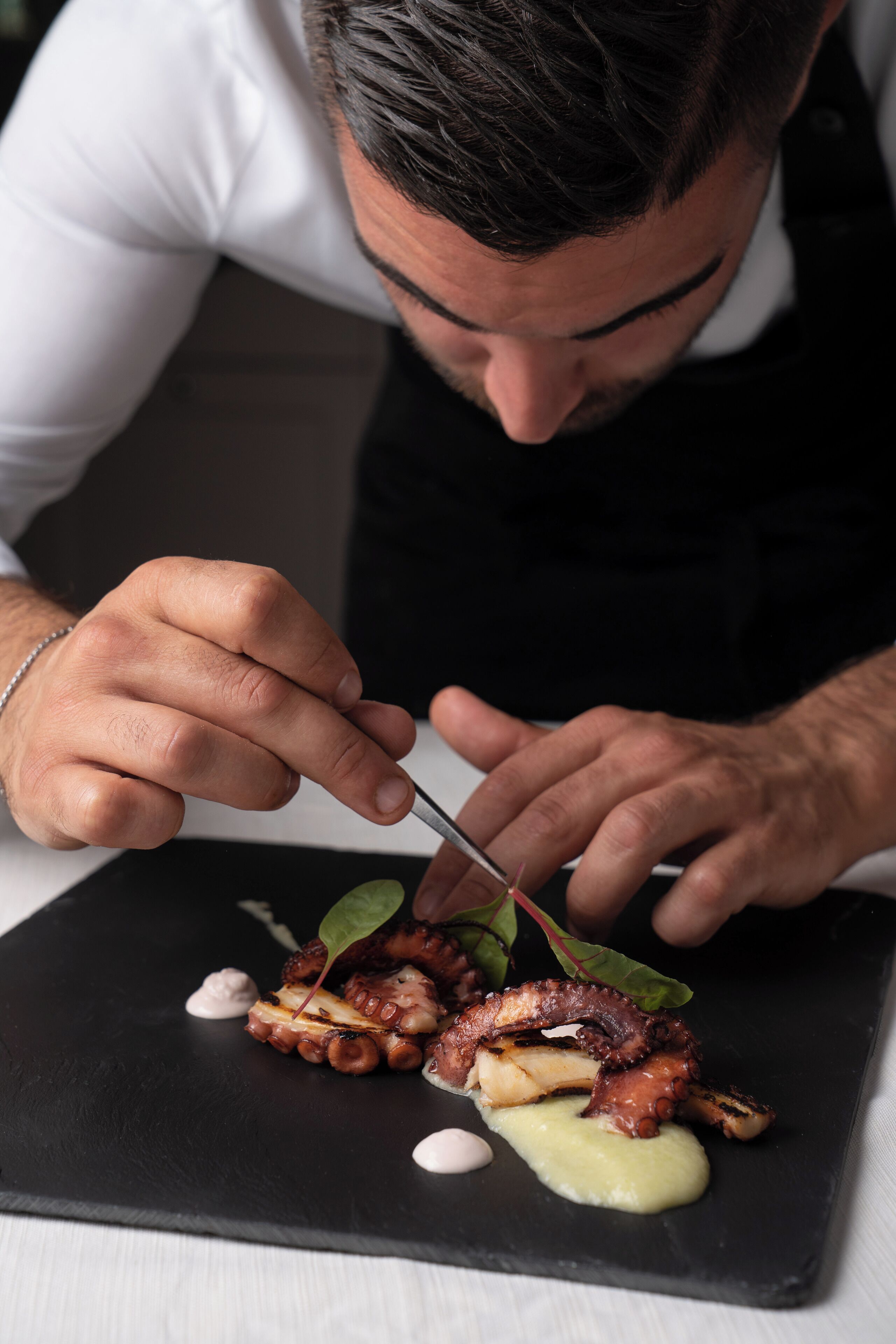 Una persona sirviendo pulpo en un plato de pizarra negra.